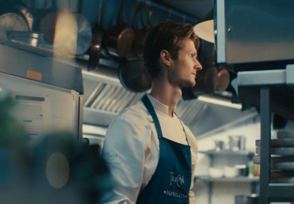 Een vrouwelijke chef-kok in een professionele keuken, die nadenkend naar haar werk kijkt.