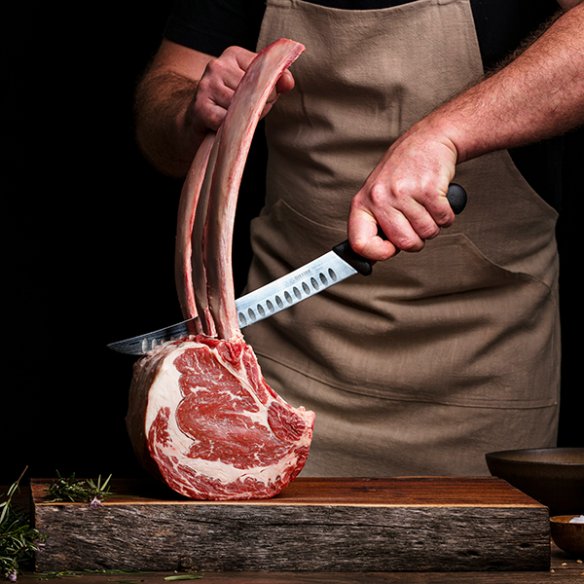 Chef découpe une côte de bœuf tomahawk en cuisine