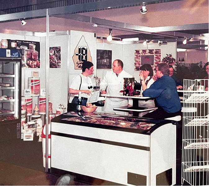 Une photo vintage en noir et blanc du magasin d'origine, avec plusieurs personnes derrière un comptoir servant les clients.