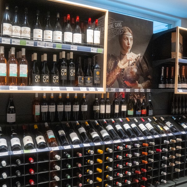 Een goed georganiseerde wijnafdeling in een winkel, met talrijke flessen wijn uitgestald op donkere houten rekken.

