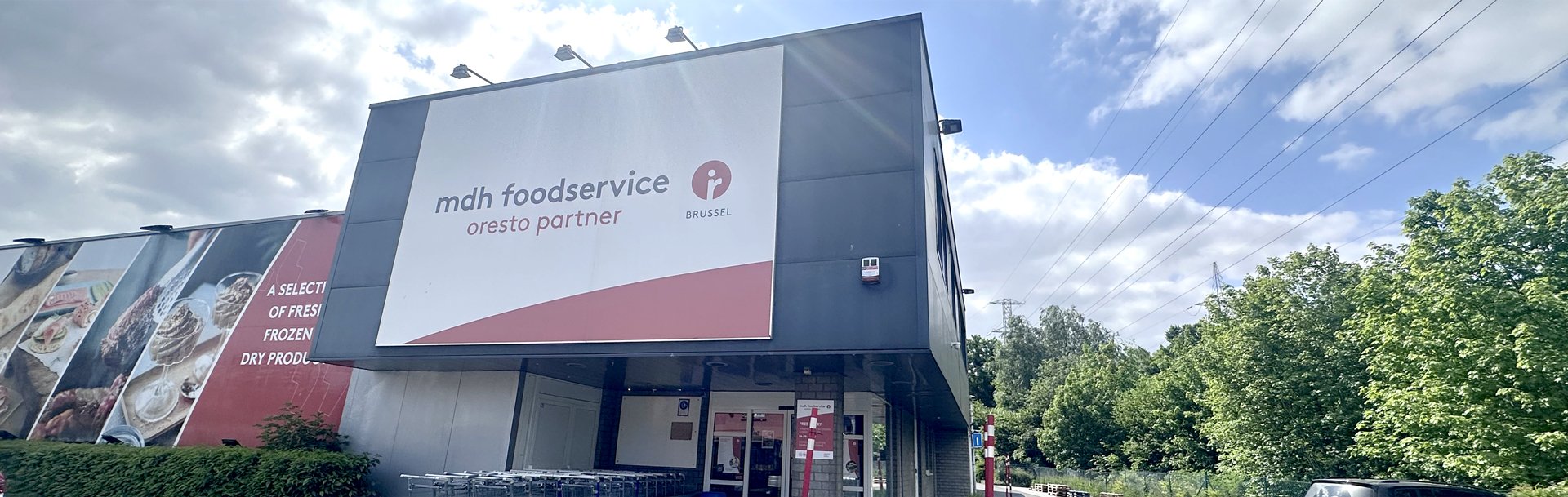 De buitenkant van het gebouw van mdh foodservice oresto partner Brussel op een zonnige dag met enkele wolken. Het is een modern, commercieel gebouw met twee verdiepingen.