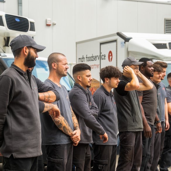 Een groep mannelijke medewerkers van mdh foodservice die buiten samen in een rij staan en aandachtig kijken.
